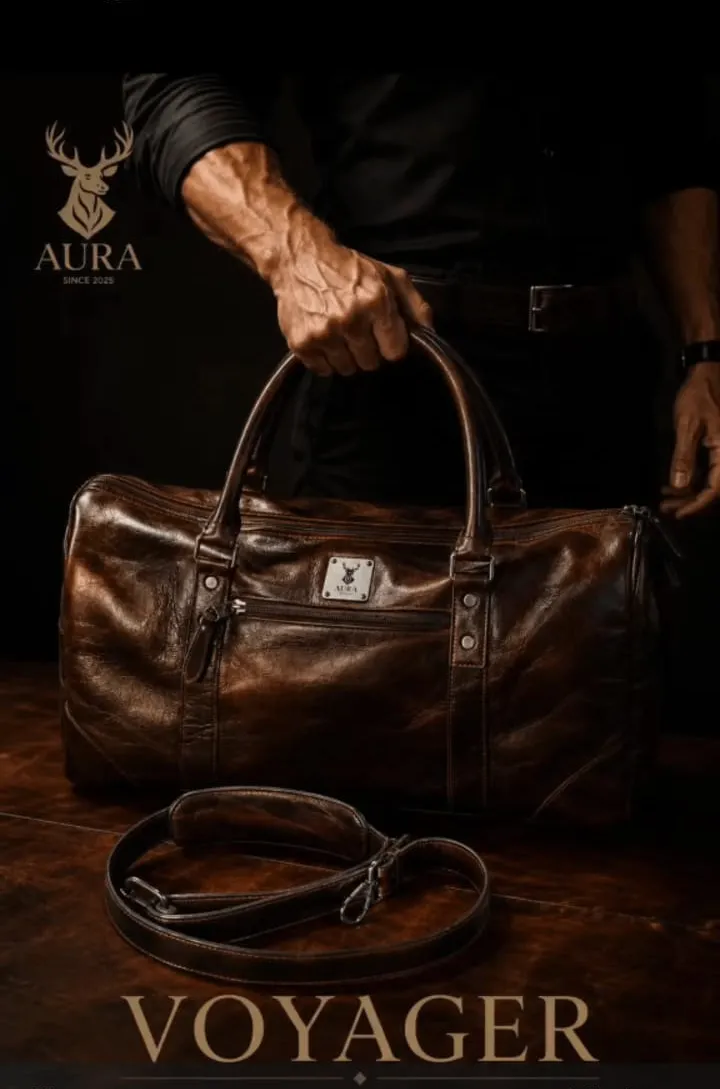 Bolso de viaje de cuero AURA VOYAGER en tabaco, iluminado sobre fondo oscuro, con las asas dobles remachadas en primer plano.